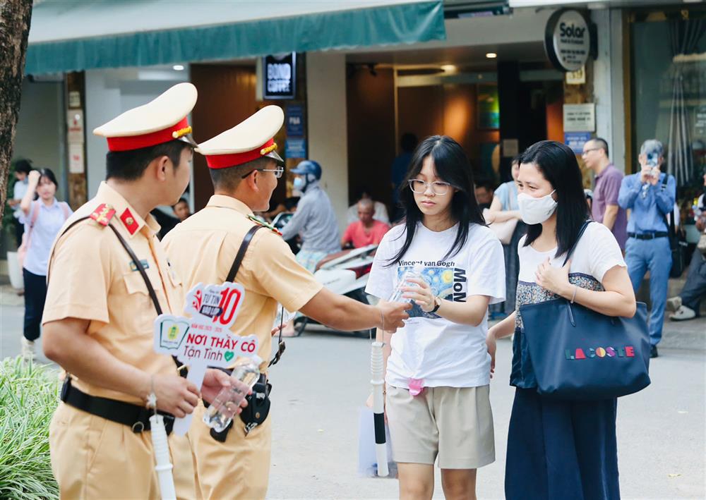 Cán bộ, chiến sĩ Công an Thủ đô phát nước uống, tài liệu ôn tập và quạt giấy cho thí sinh trước giờ vào phòng thi, thể hiện tinh thần đồng hành, sẻ chia trong mùa thi.